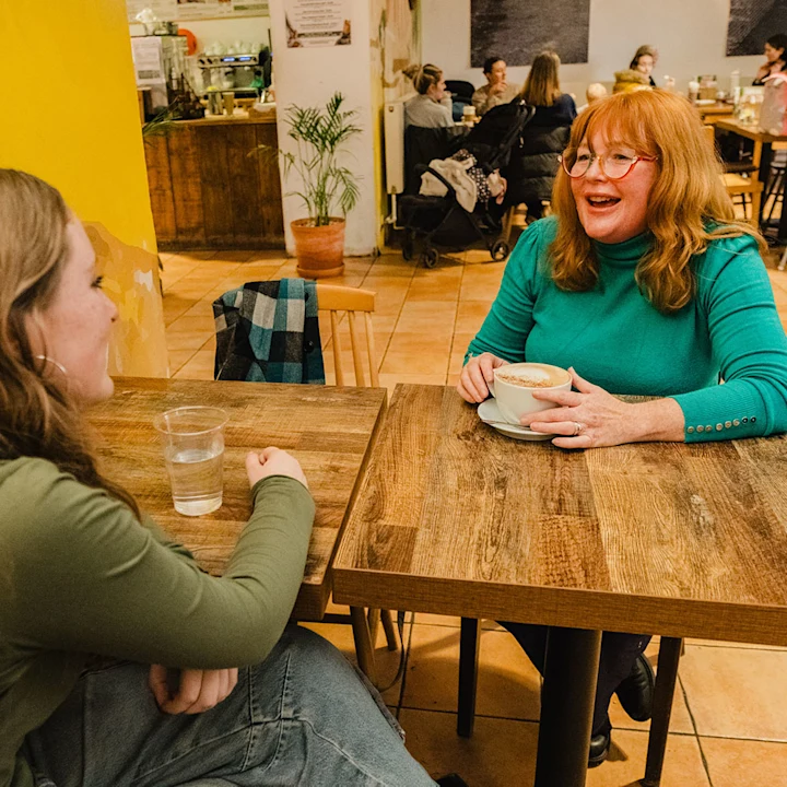 An adult woman sat opposite a young woman in a bright café setting.
