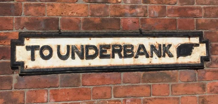 A nameplate against a brick wall reading 'To Underbank' with a a picture of a hand pointing to the right. 
