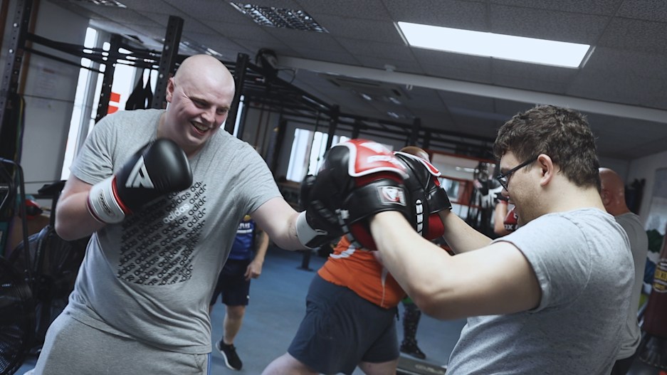 Men boxing using gloves and boxing pads.