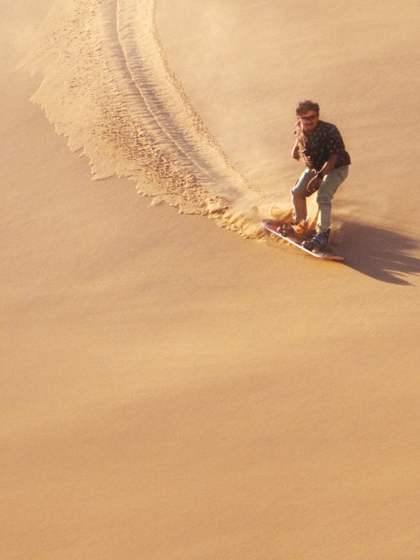Karim åker sandboard nerför en gyllene sanddyn, lämnar ett långt spår och kastar en dramatisk skugga över ökensanden.