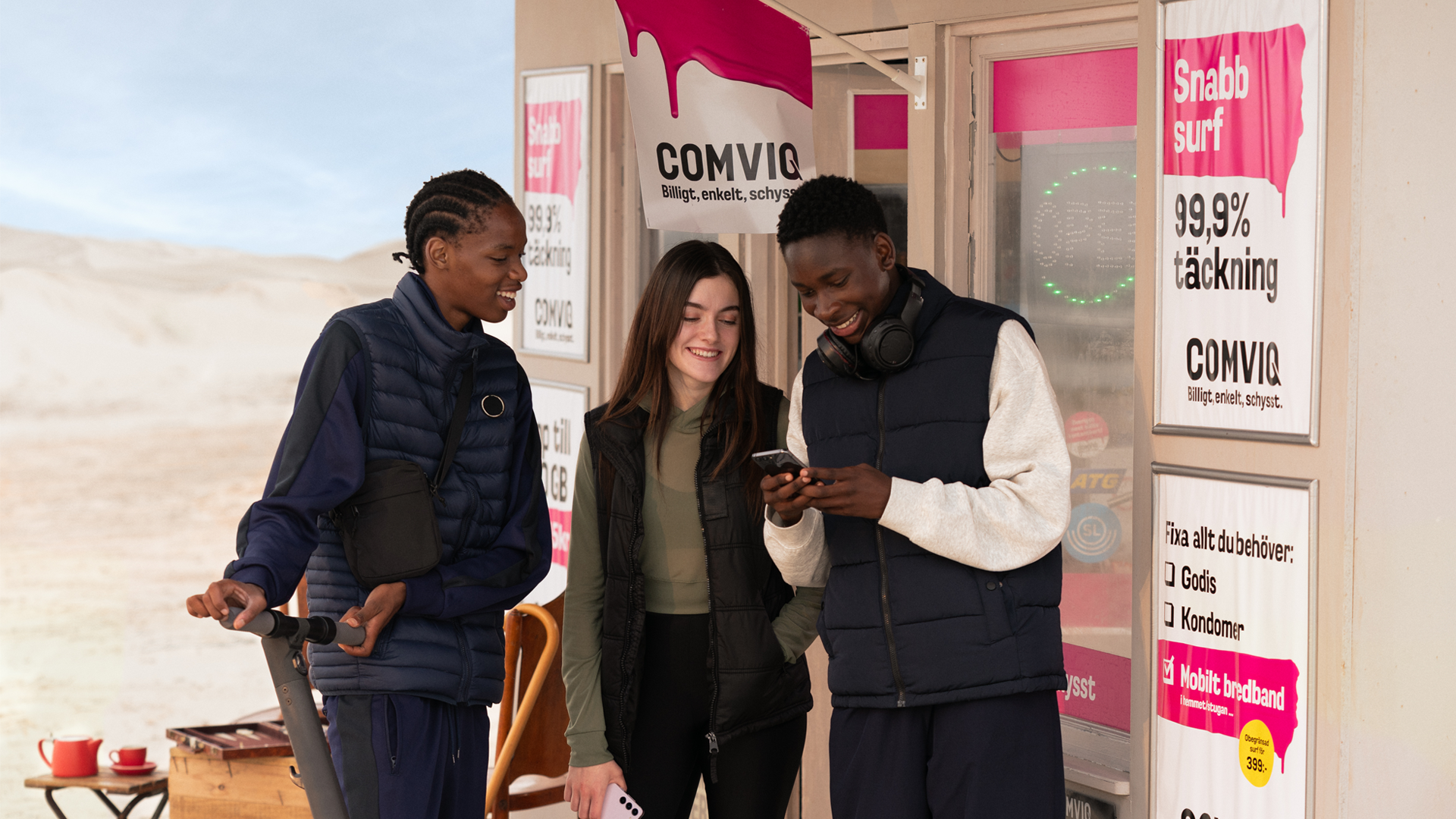 Tre tonåringar står utanför Comviq-kiosken och ler åt något de ser i mobilen