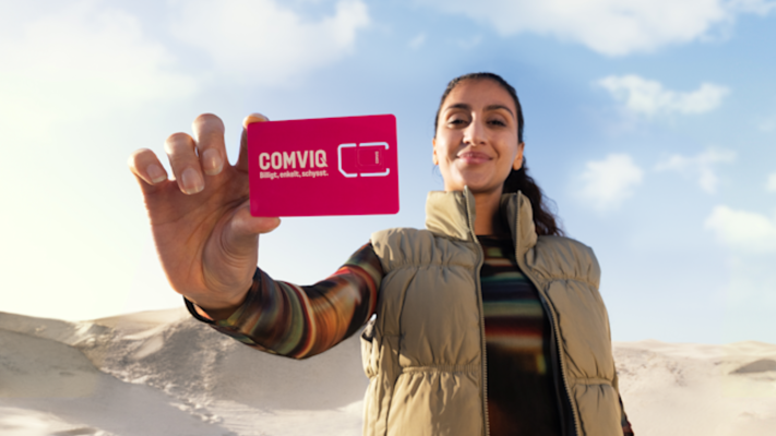 Nadja håller fram i ett kontantkort med Comviq-logotyp i förgrunden, i bakgrunden ökenmiljö och blå himmel 