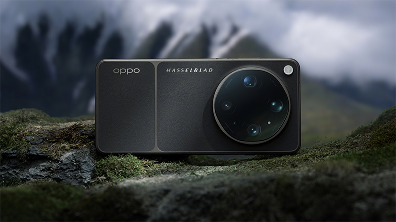 Svart OPPO-smartphone med Hasselblad-kamerasystem på baksidan, placerad på mossa med dimmiga berg i bakgrunden.