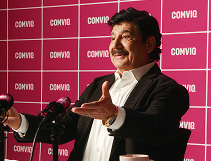 Karim i kostym talar vid presskonferens framför rosa COMVIQ-bakgrund med mikrofoner i förgrunden.
