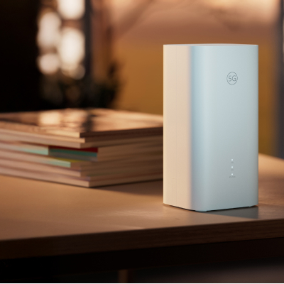 En vit rektangulär enhet med en logotyp och ljusindikatorer står på ett träbord bredvid en stapel böcker i varmt ljus.