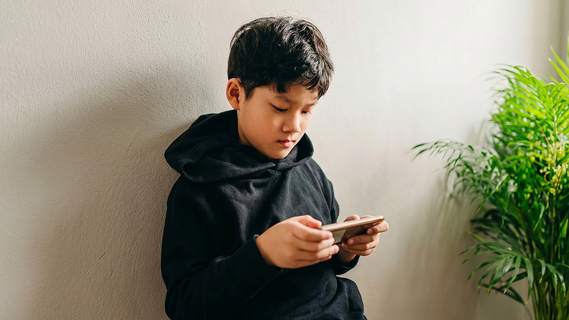 Pojke som står mot en vägg med mobil i handen