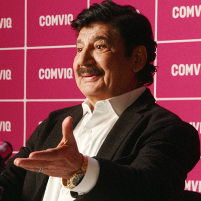 Karim i kostym talar vid presskonferens framför rosa COMVIQ-bakgrund med mikrofoner i förgrunden.