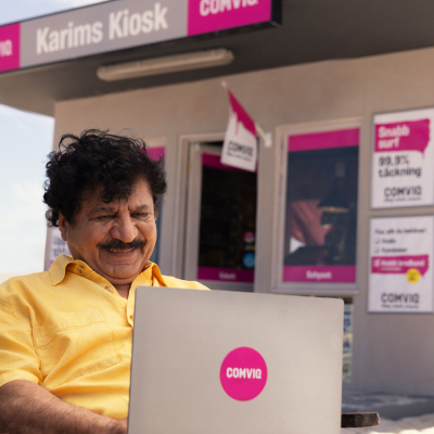 Karim sitter med sin laptop i knät utanför Comviq-kiosken och ser nöjd ut.