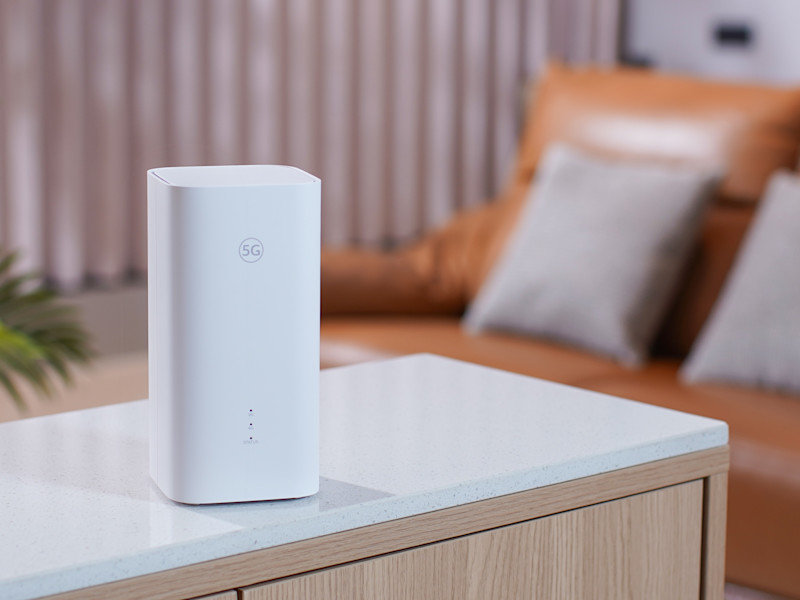 En vit, modern 5G-router stående på en ljus bänk med ett vardagsrum i bakgrunden.