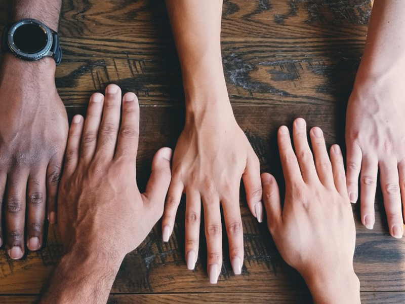 Three individuals hands placed on a wooden table to represent diversity and community