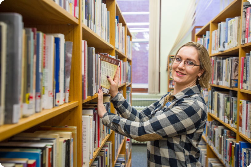 Female librarian placing a book on a bookshelf.