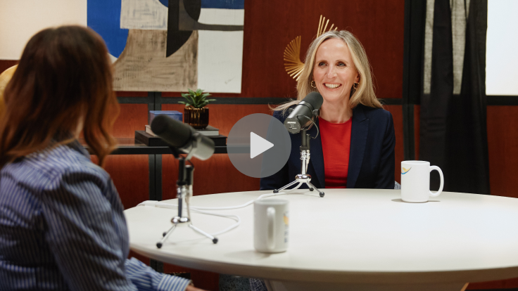Two women sitting at a table with microphones and coffee mugs