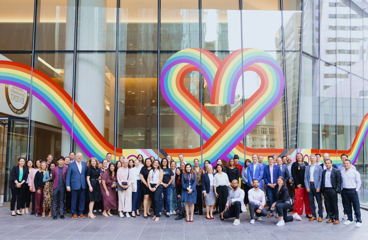 A group of people standing in front of a rainbow heart on a wall