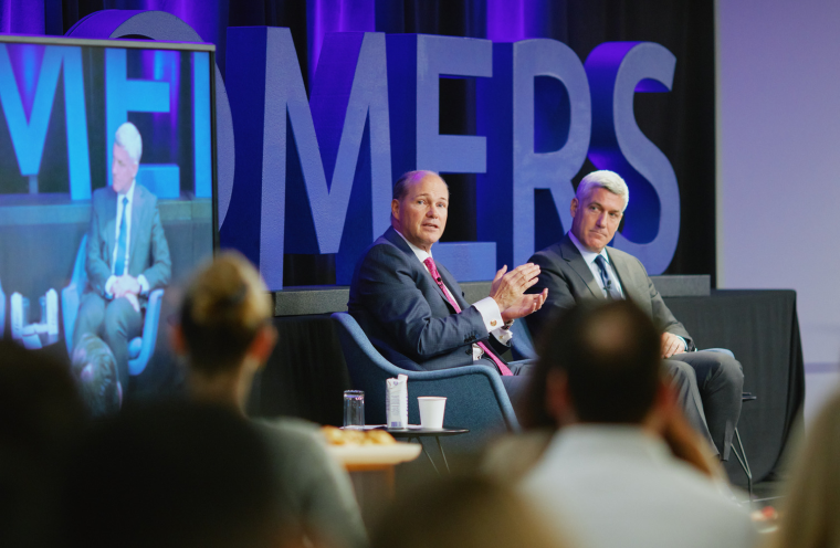 two men sitting and speaking to a crowd