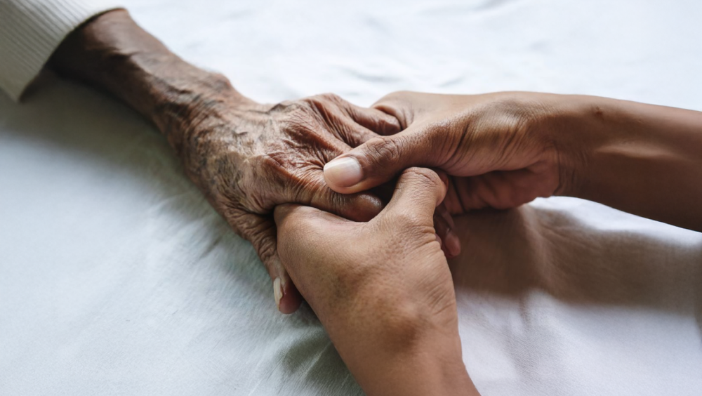 Two adult hands holding the hand of an elderly person