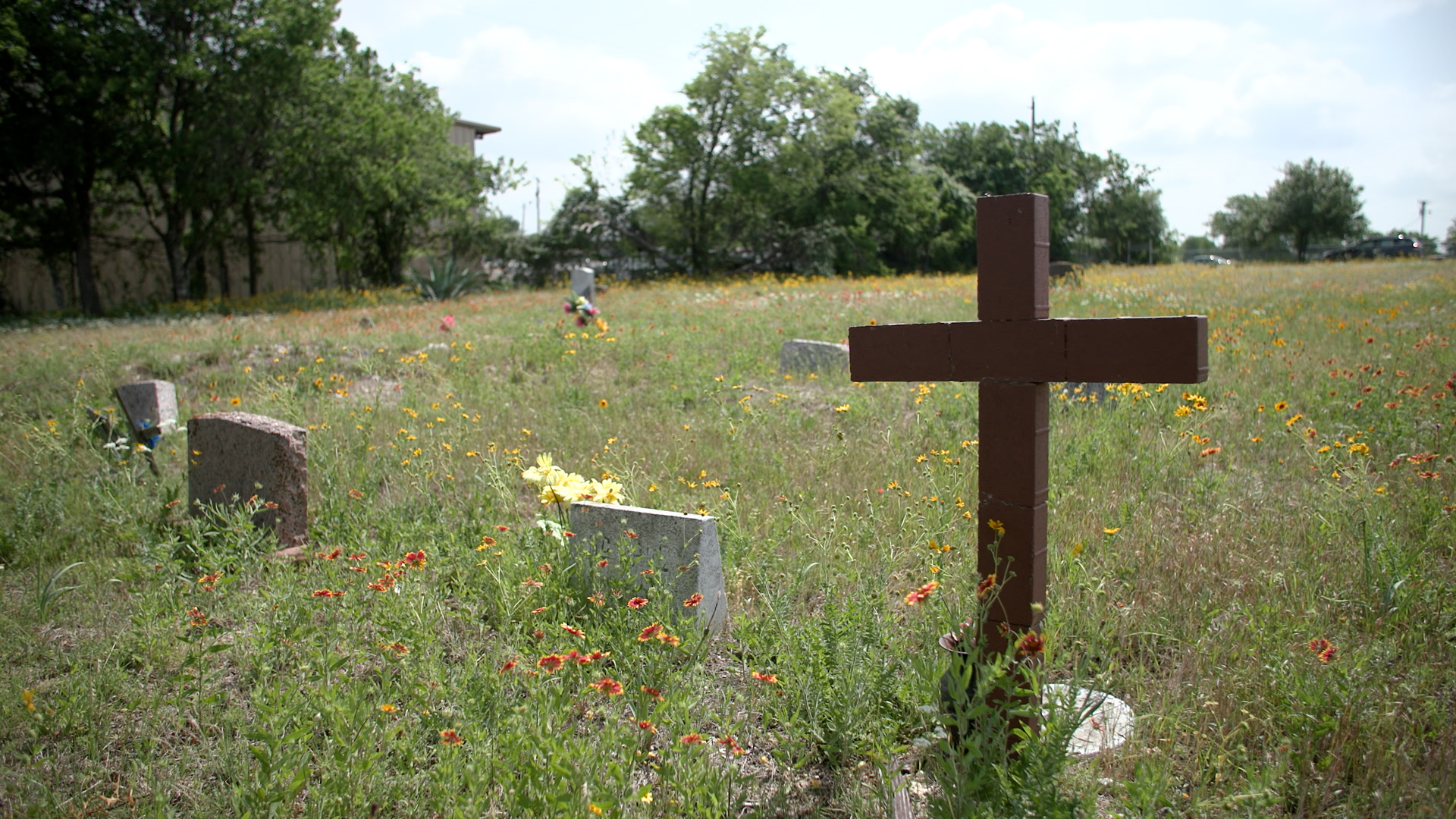 Three headstones and a brick cross mark the graves of those interred at the cemetery within the Pflugerville Colored Addition. As families have left the area, cemetery upkeep has fallen by the wayside, an issue seen across the country for historically Black cemeteries.