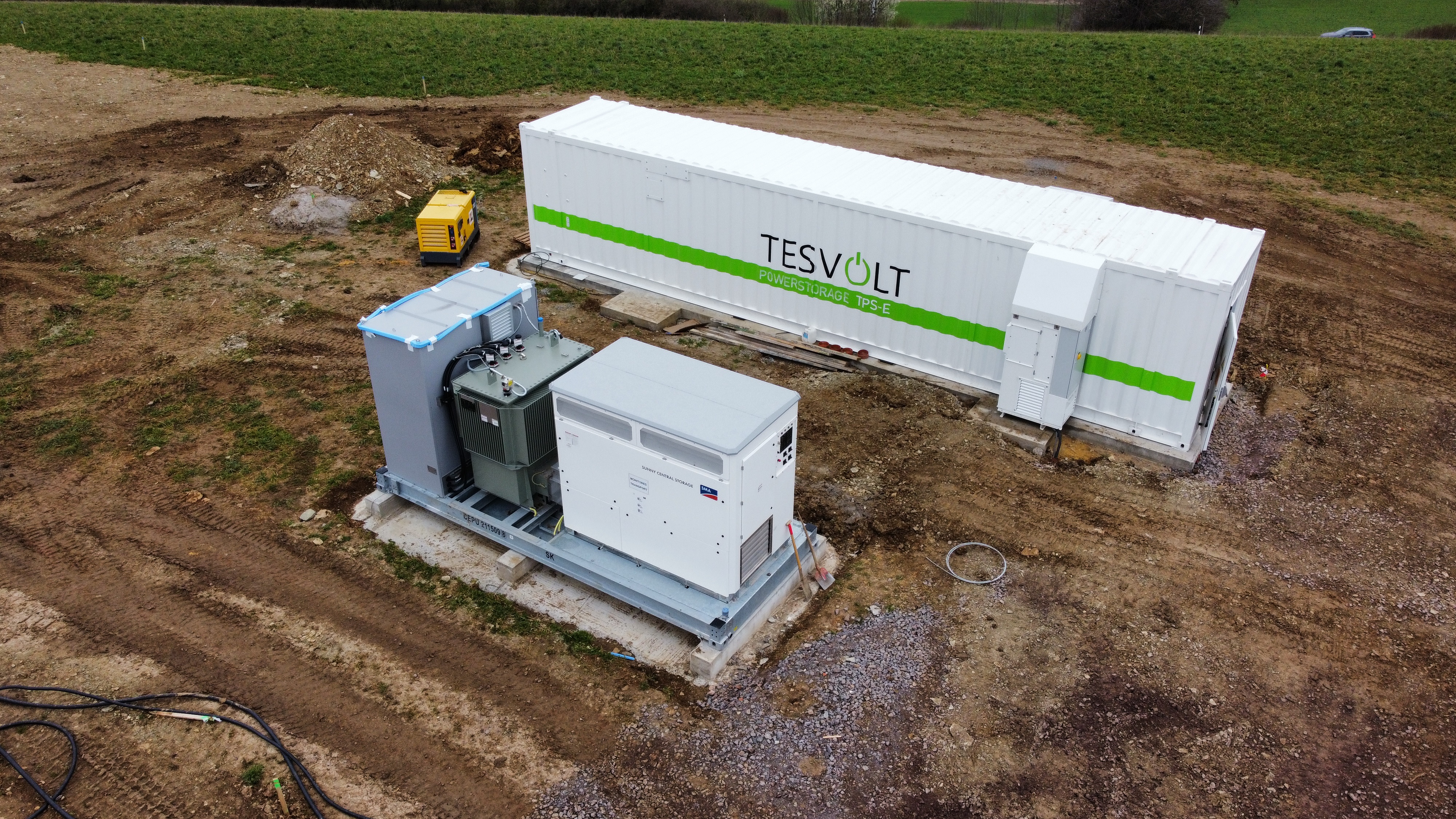 In the picture, a large white battery storage system is shown in an open field.