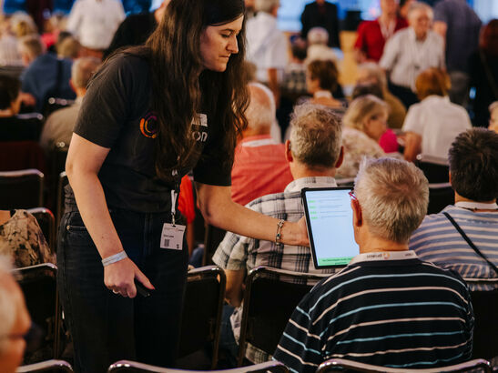 Eine Prokon-Mitarbeiterin reicht einem Mitglied das Abstimmungs-Tablet bei der Generalversammlung 2024 