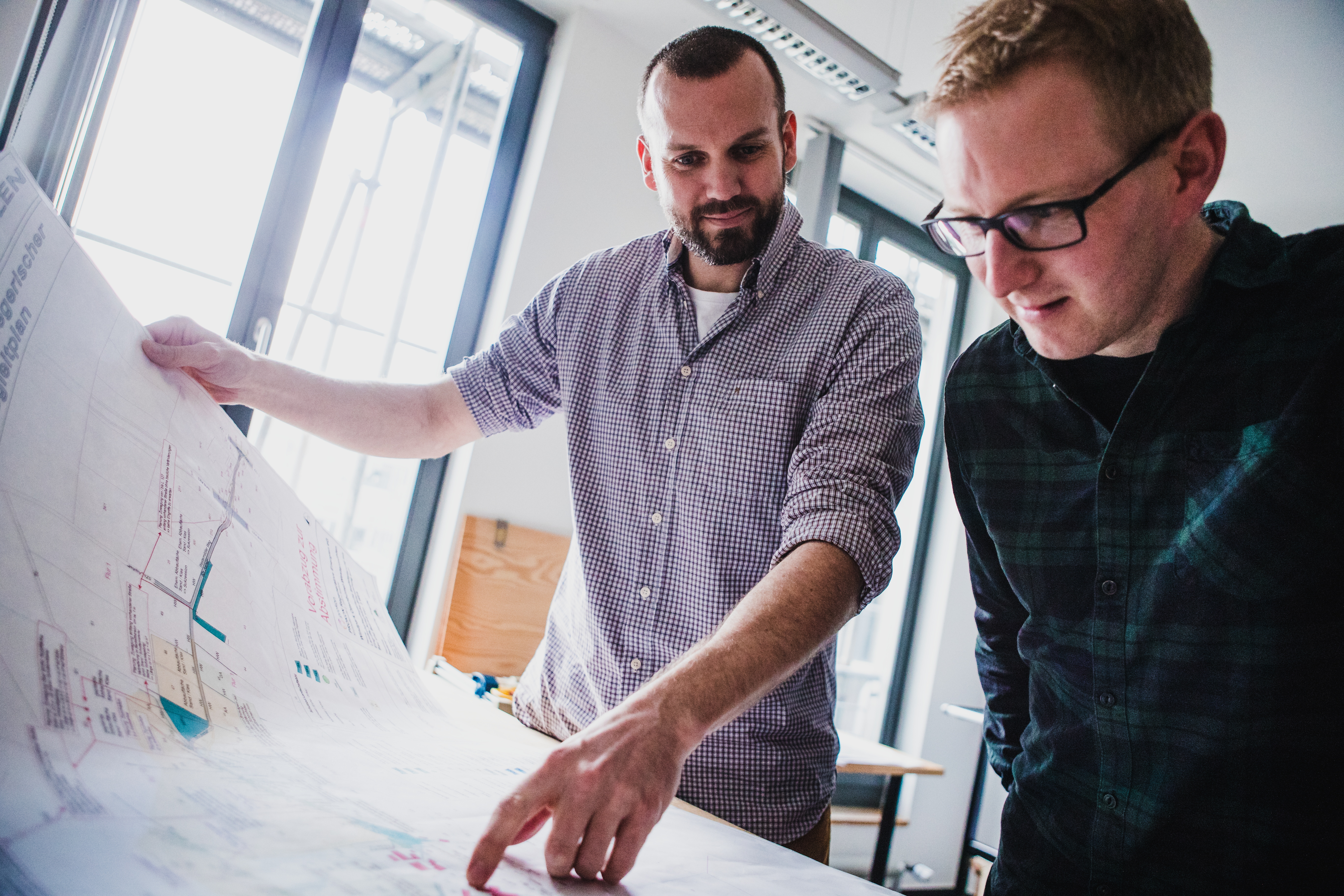 Auf dem Foto sind zwei Projektentwickler dargestellt, die gemeinsam einen Plan betrachten.