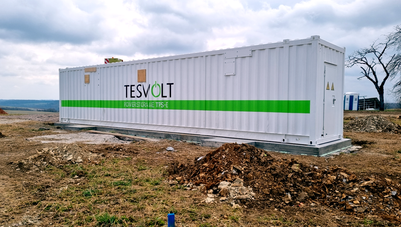 Auf dem Bild ist ein großer Batteriespeicher des Herstellers Tesvolt abgebildet, der auf einer Freifläche steht.