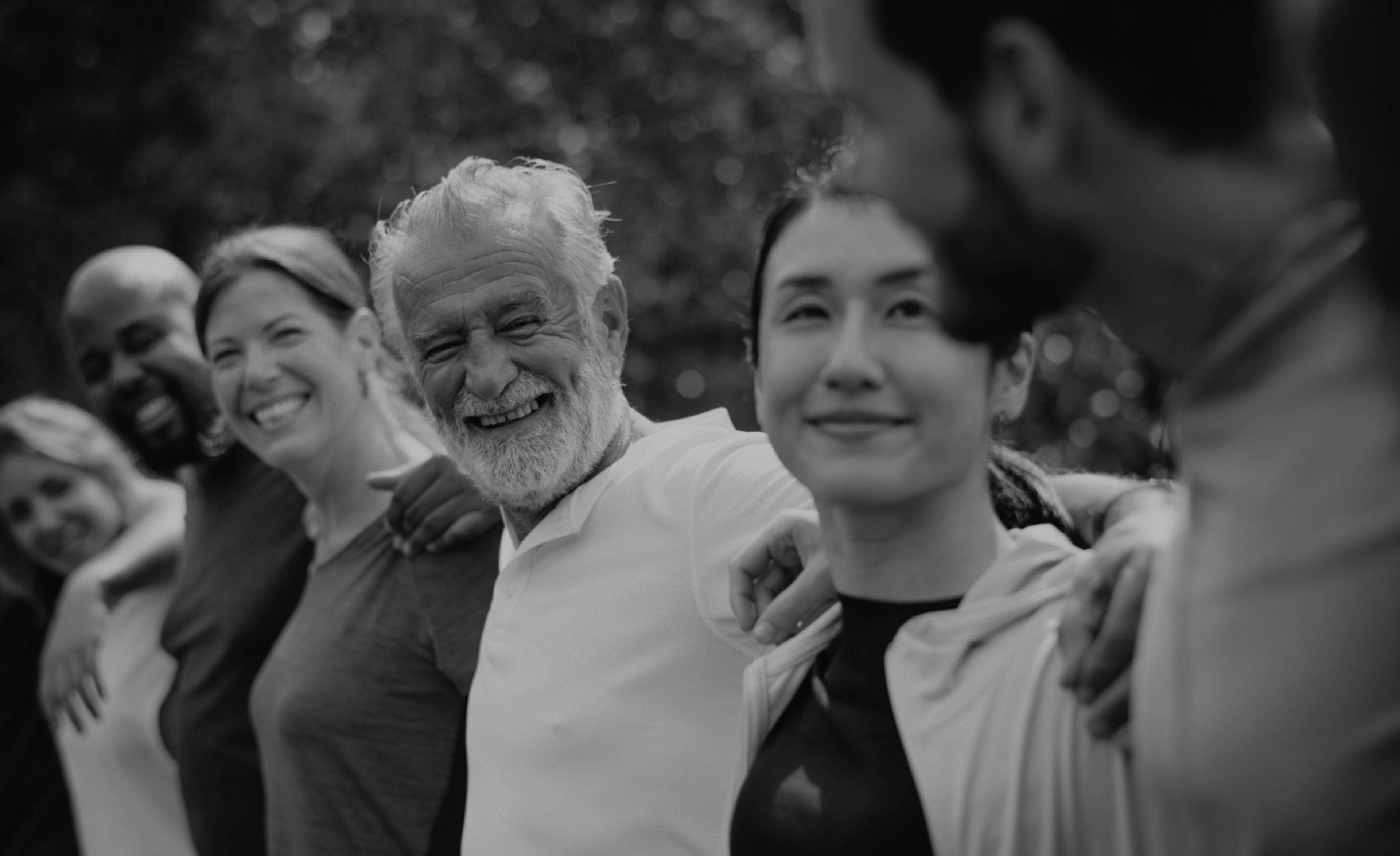 Group of diverse people standing together with arms over each others shoulders.