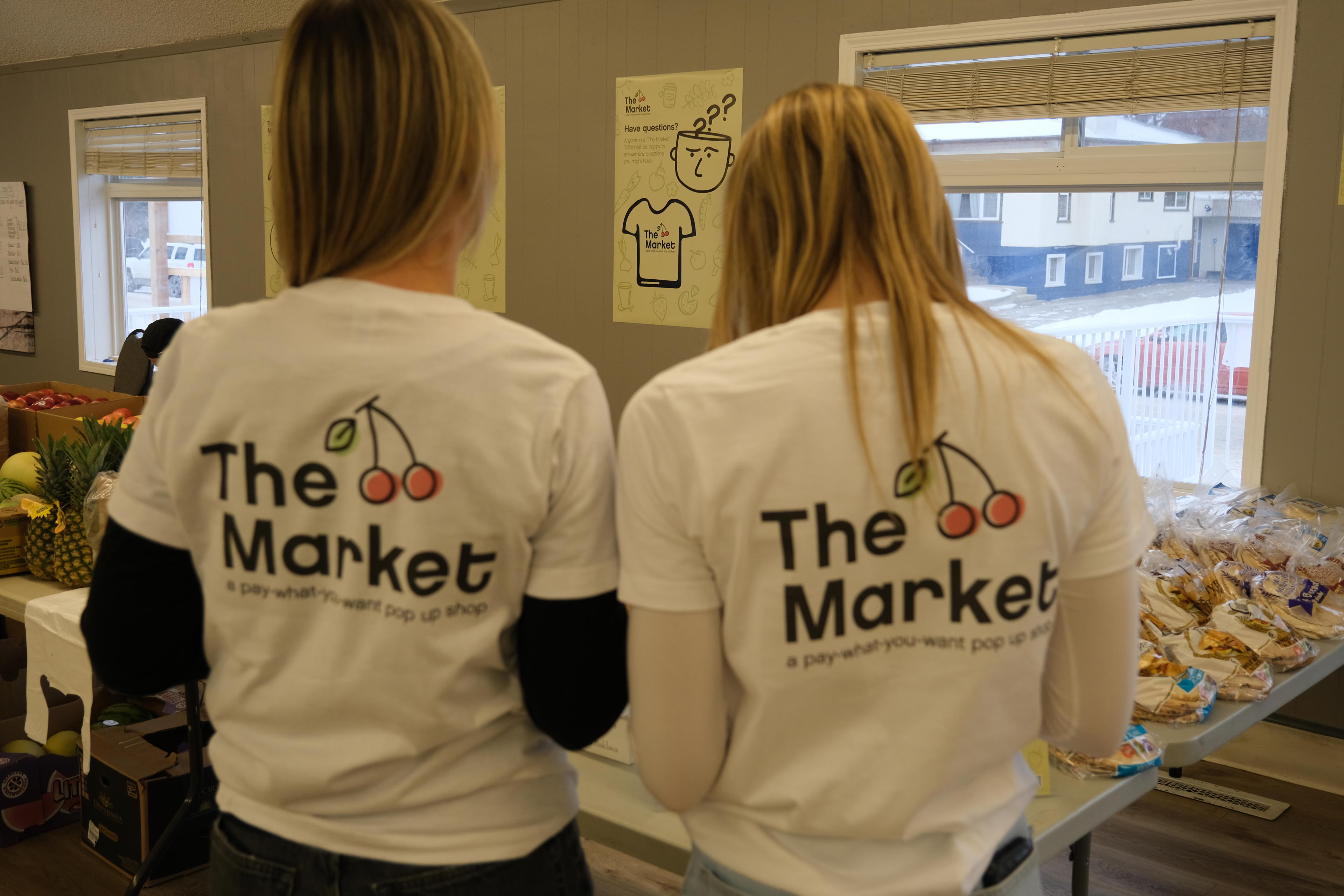 2 girls standing with their backs to the camera with matching shirts that say "The Market".