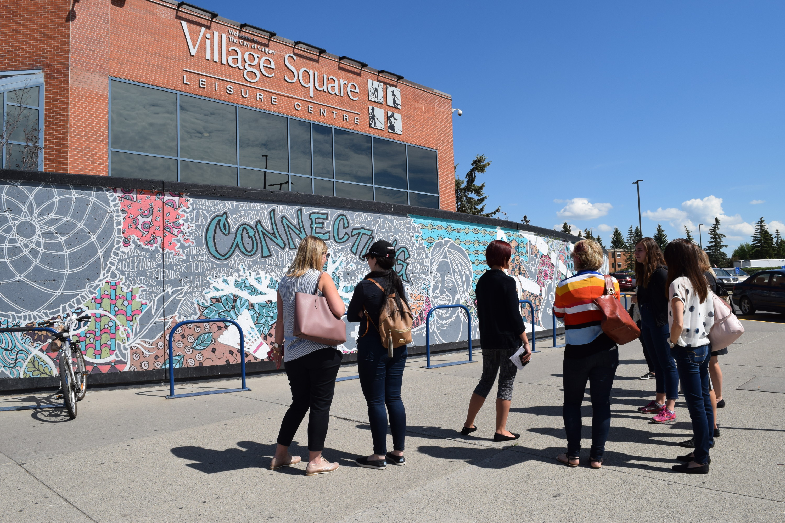 Group of teens standing on cement walkway with an artistic painted wall of patterns and the word"connecting" in the background.