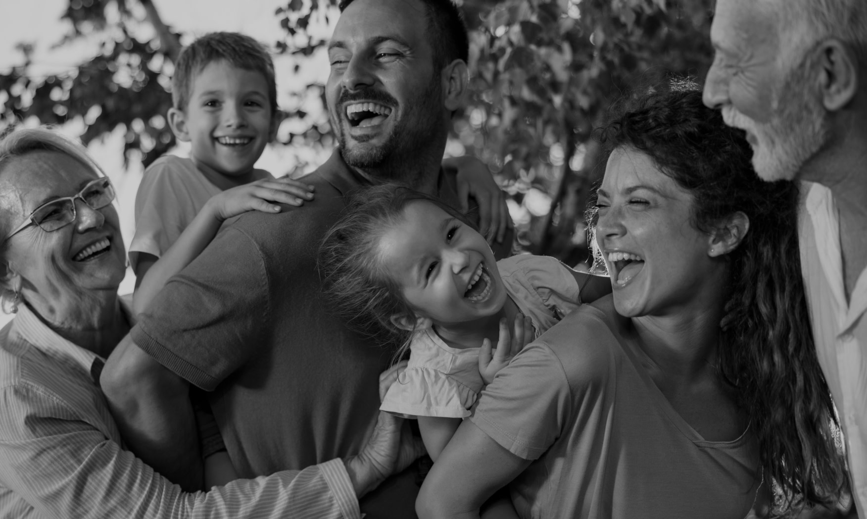 Closeup photo of parents, with kids on their backs and grandparents on either side. The family is laughing and posed in a playful manner.