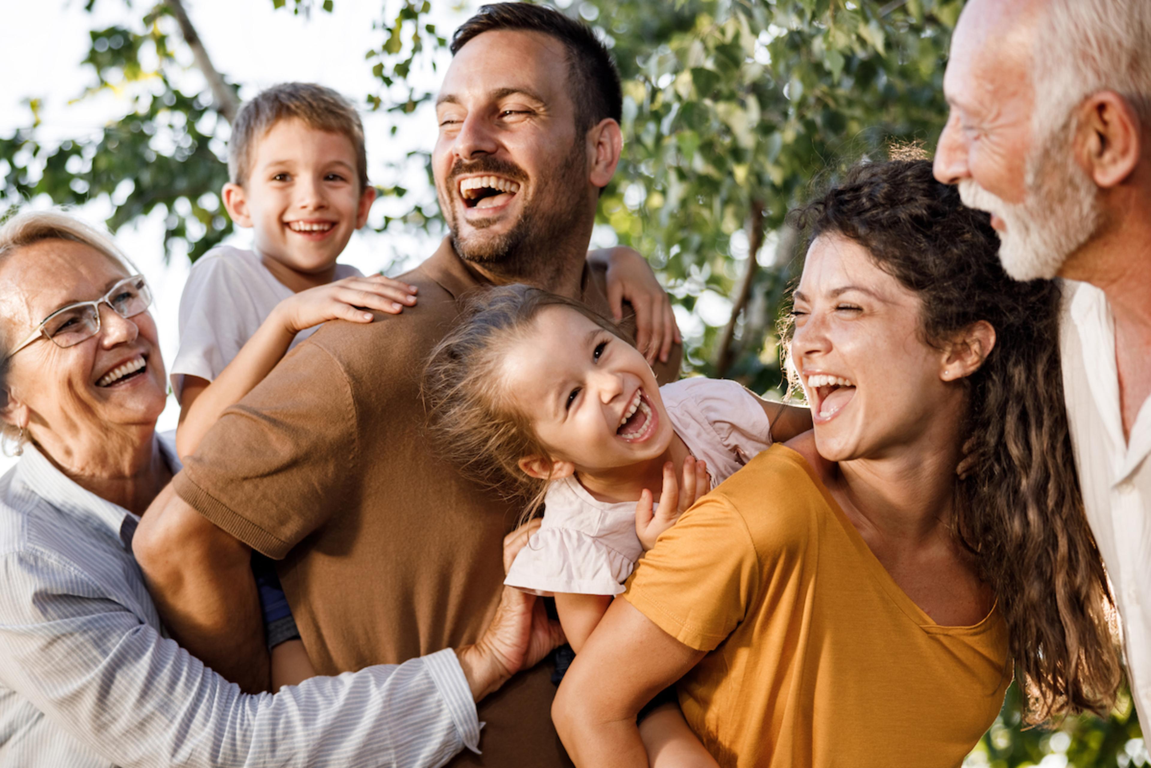 A family giving their children piggyback rides while grandparents watch.