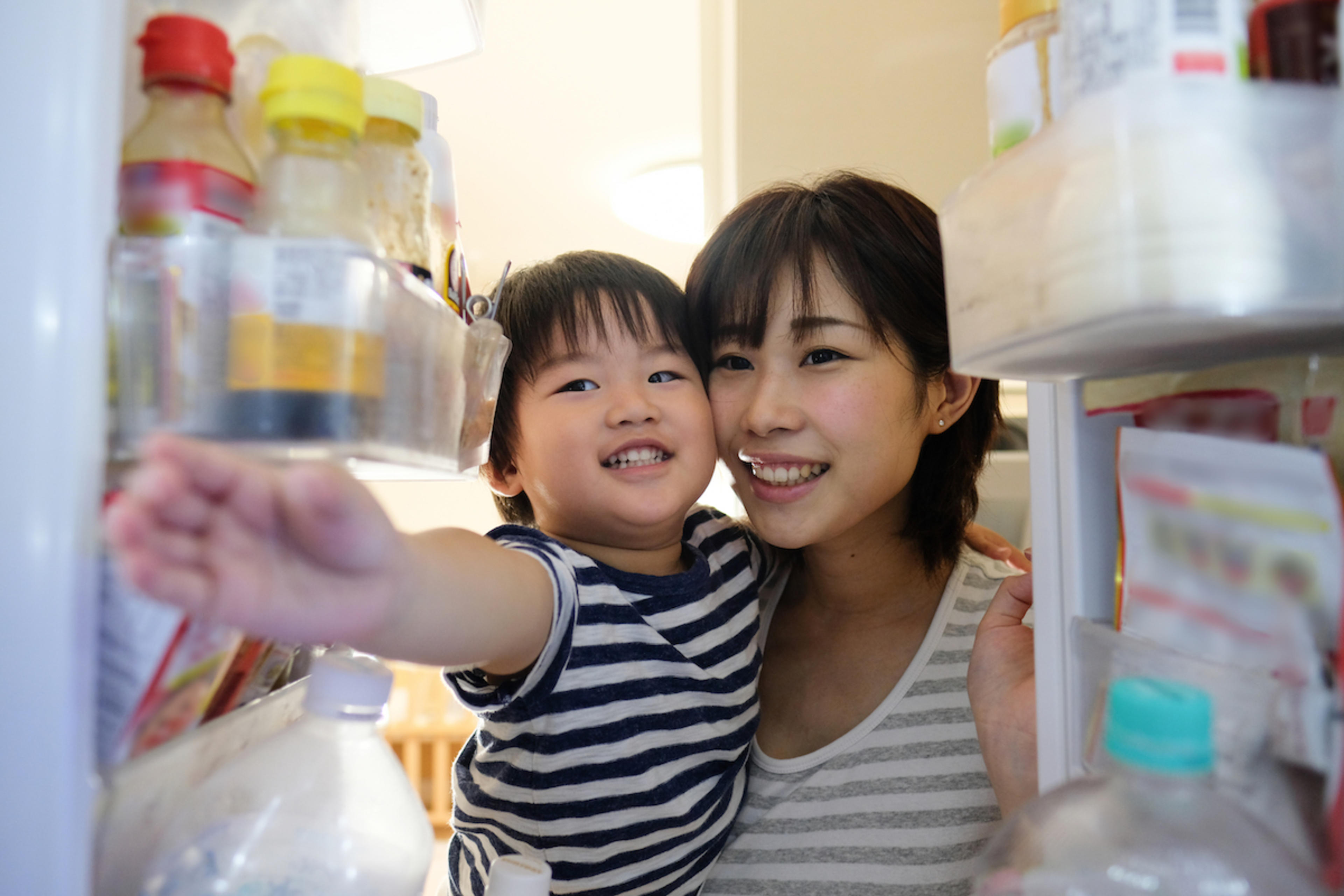 A woman and her child look into a refrigerator. 