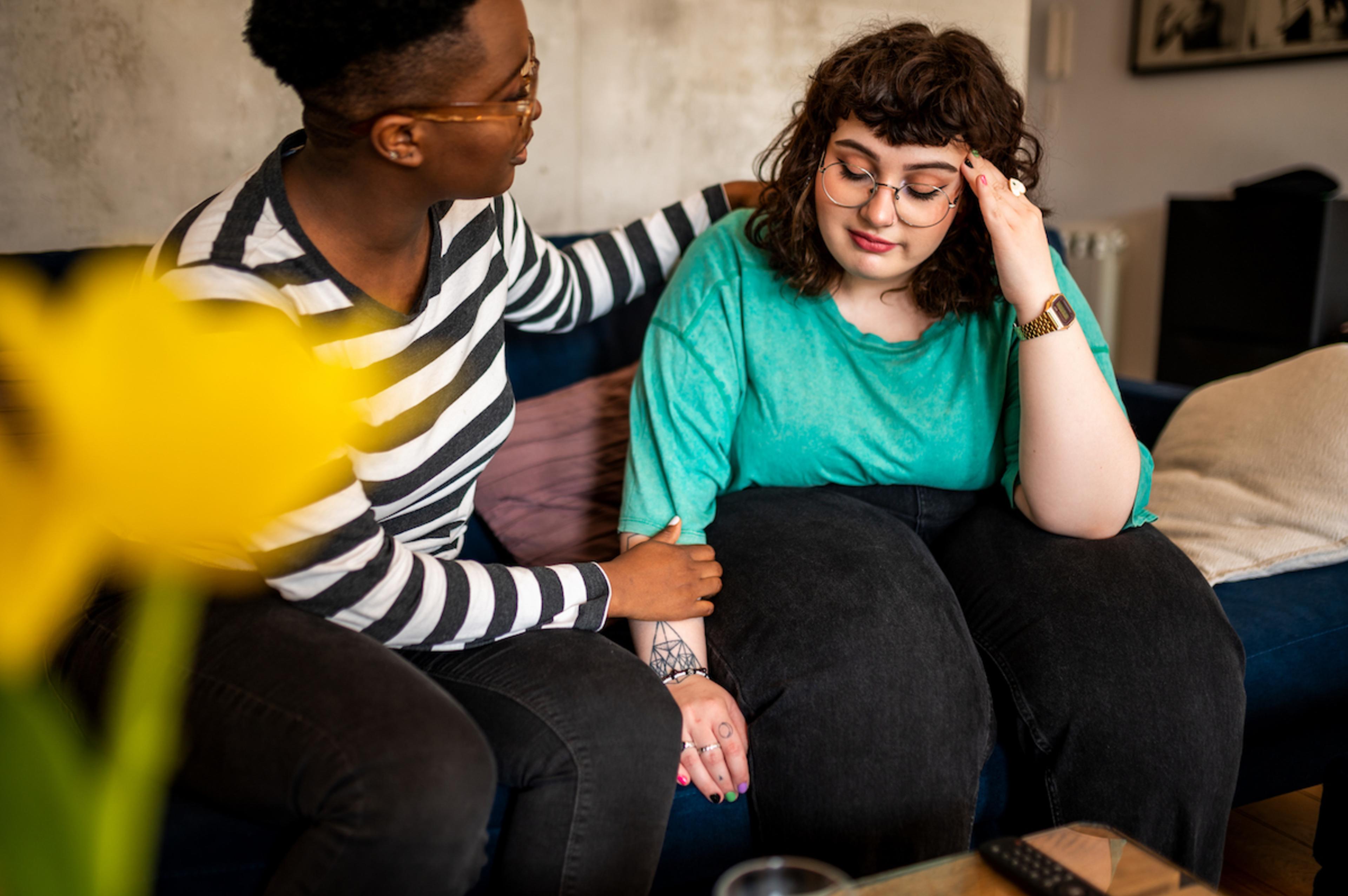 Woman with her hand on her head being supported by a friend.