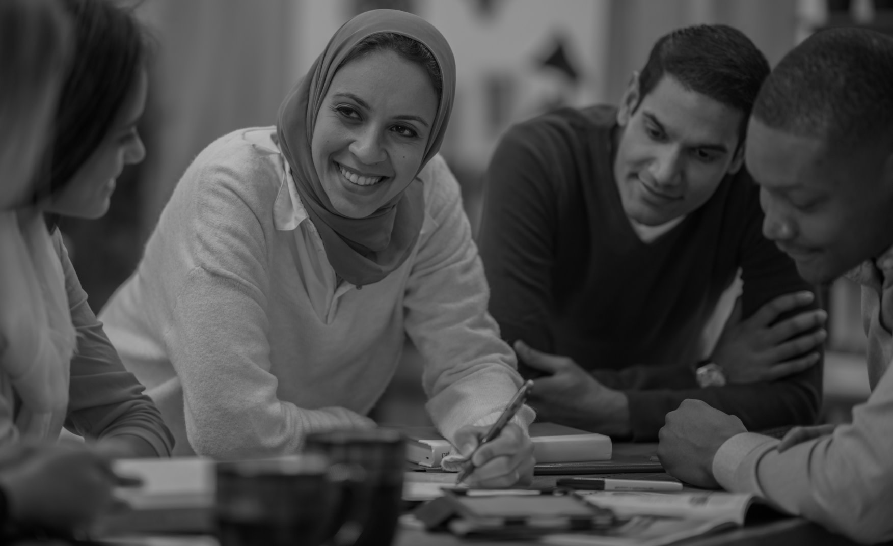 Group of 4 people working at a desk together. 