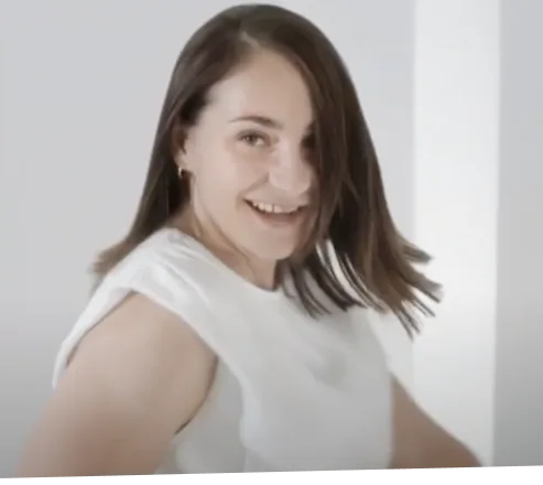 Kobieta uśmiechająca się do aparatu. Ma na sobie białą bluzkę.