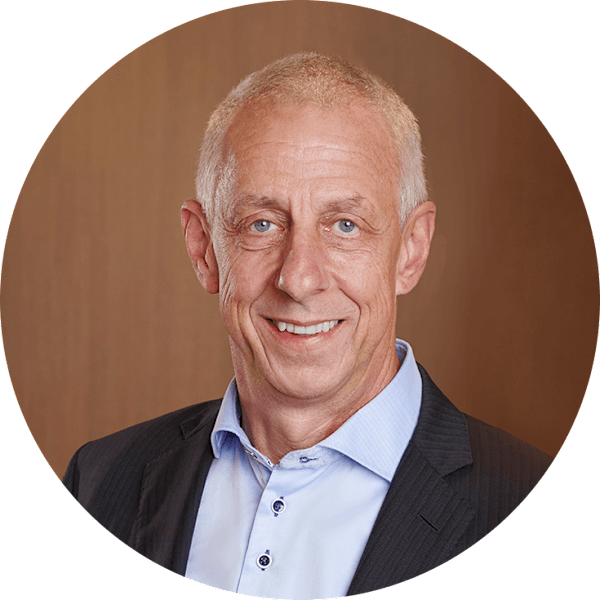 Mężczyzna uśmiecha się do kamery. Ma na sobie jasnoniebieską koszulę i czarną marynarkę.