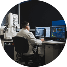 Mężczyzna w białym fartuchu siedzi przy biurku w swoim laboratorium i analizuje wiele danych na ekranach komputerowych.