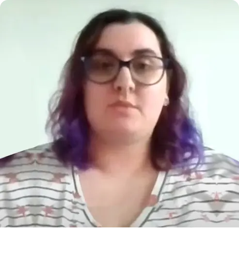 Kobieta patrząca w stronę aparatu. Ma na sobie okulary i długie, falowane włosy.