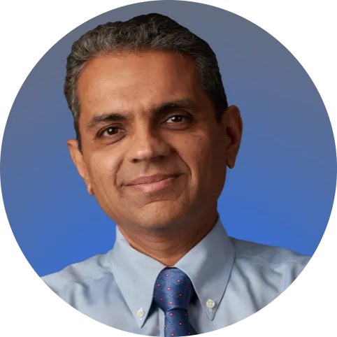 Bala Purushothaman, Chief Human Resources Officer, lekko uśmiecha się do kamery. Ma na sobie jasnoniebieską koszulę i ciemnoniebieski krawat.