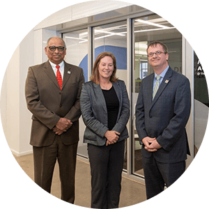 Kobieta i dwóch mężczyzn w garniturach stoją razem, uśmiechają się i patrzą w kamerę