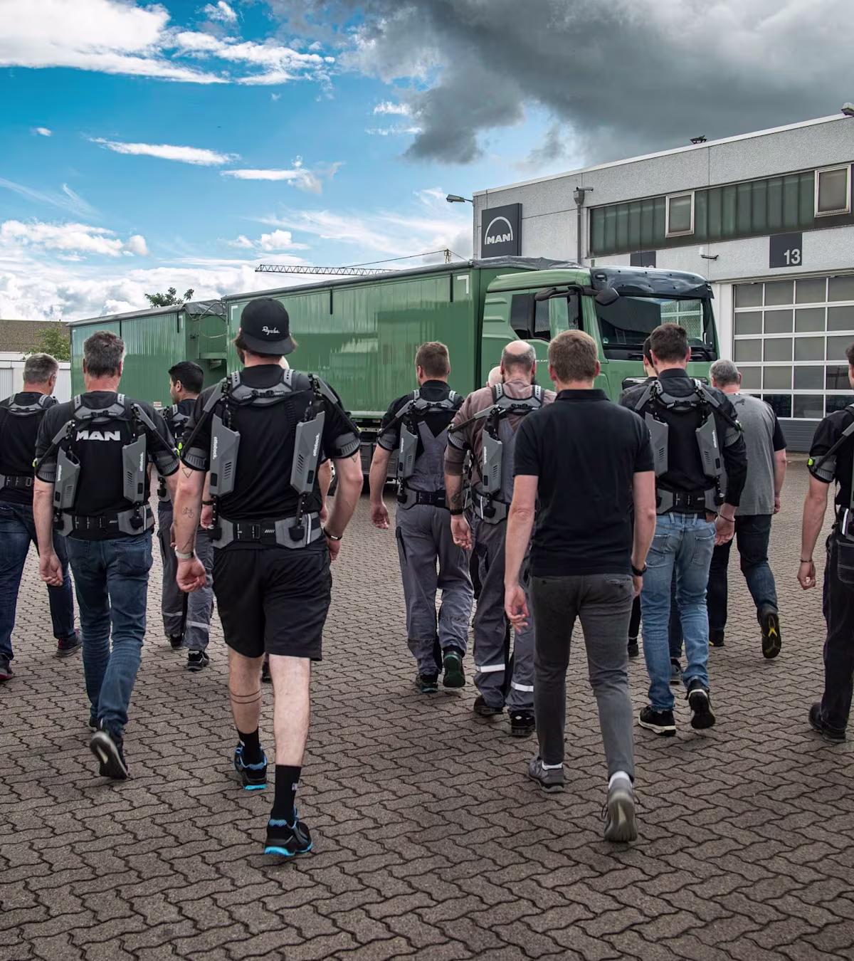 MAN mechanics wearing IX SHOULDERs from SUITX walk across the yard to the truck workshops.