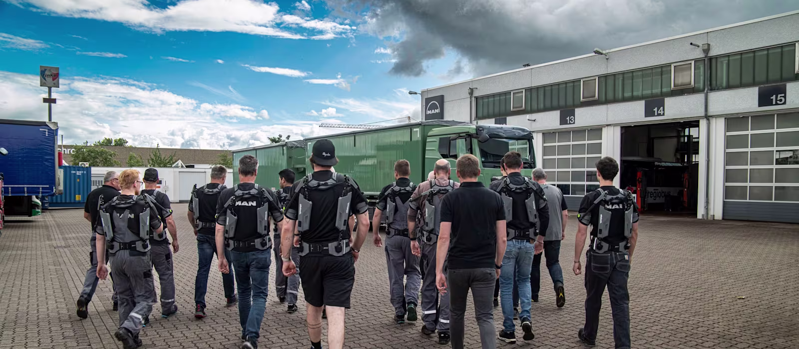 MAN mechanics wearing IX SHOULDERs from SUITX walk across the yard to the truck workshops.