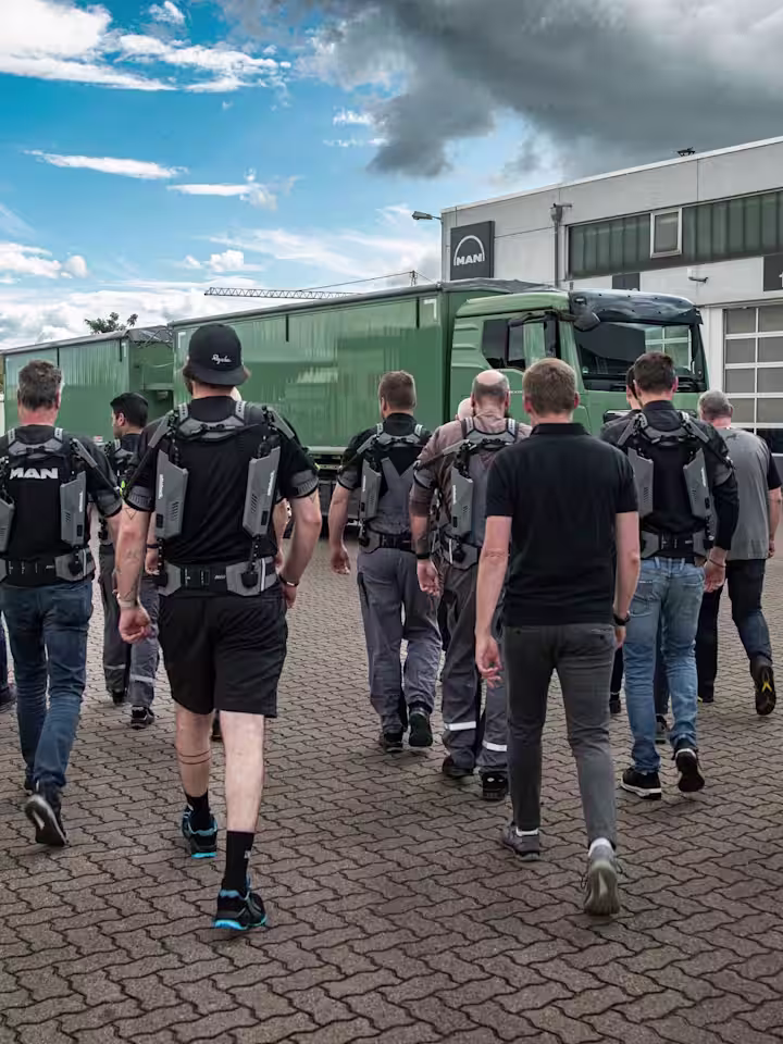 MAN mechanics wearing IX SHOULDERs from SUITX walk across the yard to the truck workshops.