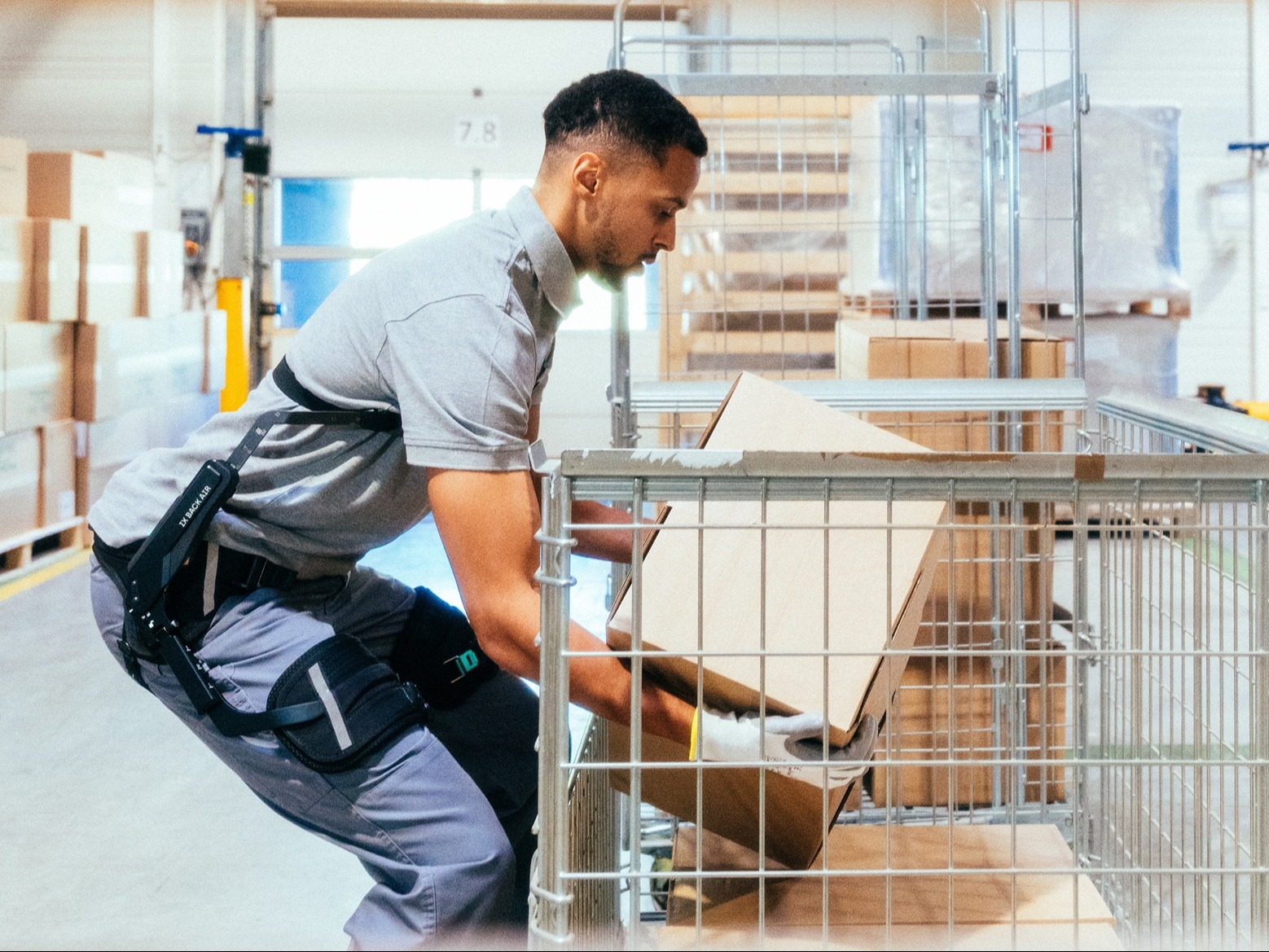 Partial view of a employee in logistics wearing the IX BACK AIR back exoskeleton and lifting a box.