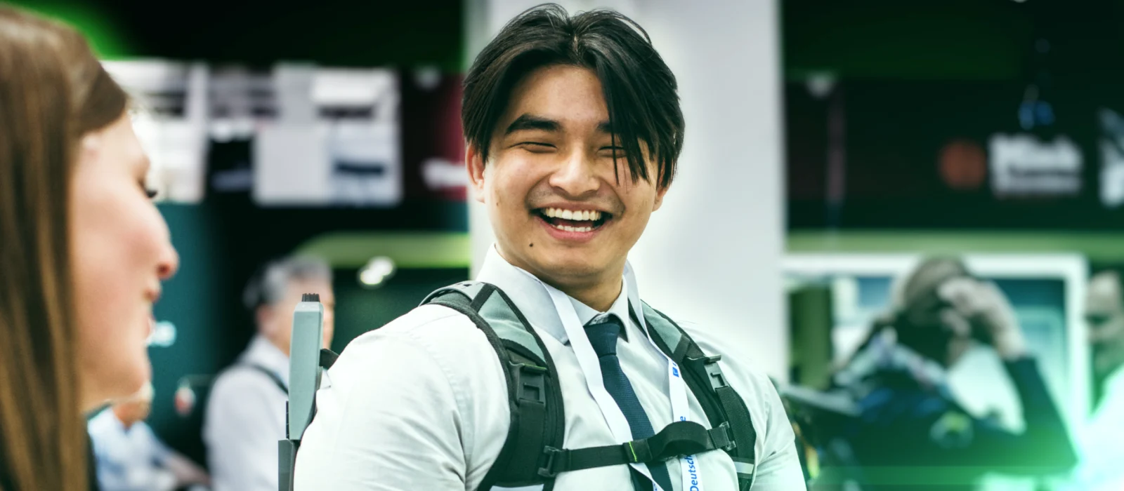 Male person wearing a SUITX exoskeleton at a trade show and smiling while talking to a woman in the foreground