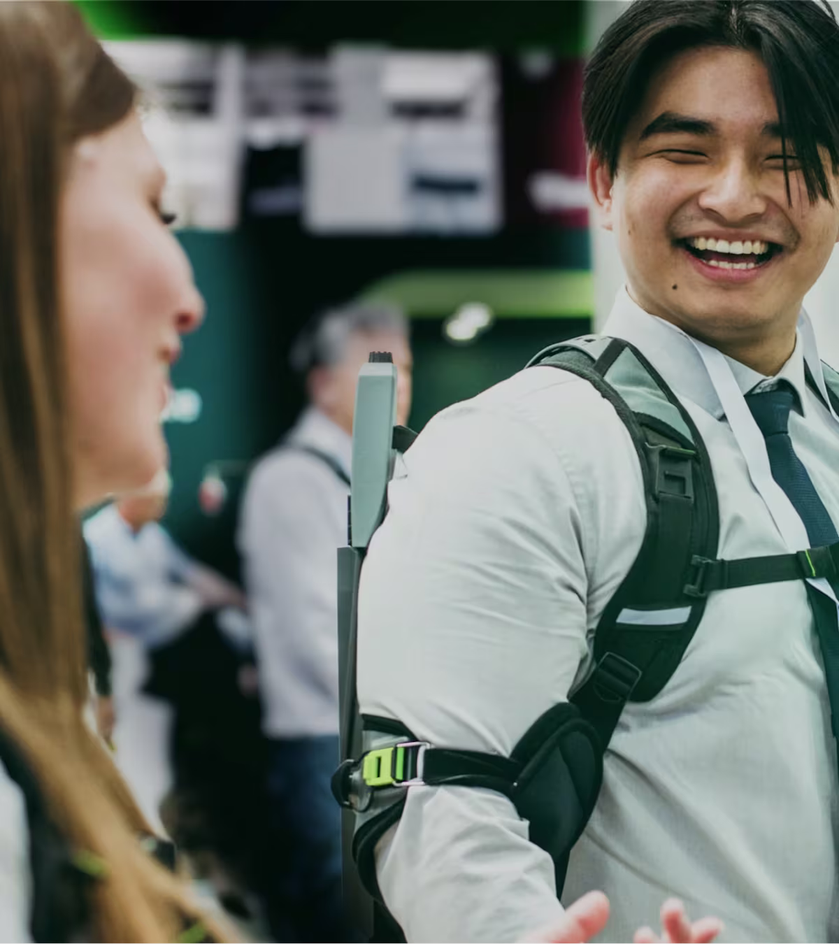 Male person wearing a SUITX exoskeleton at a trade show and smiling while talking to a woman in the foreground