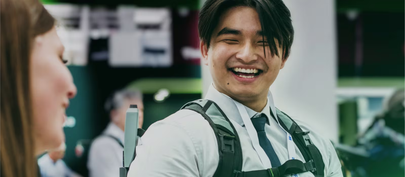 Male person wearing a SUITX exoskeleton at a trade show and smiling while talking to a woman in the foreground