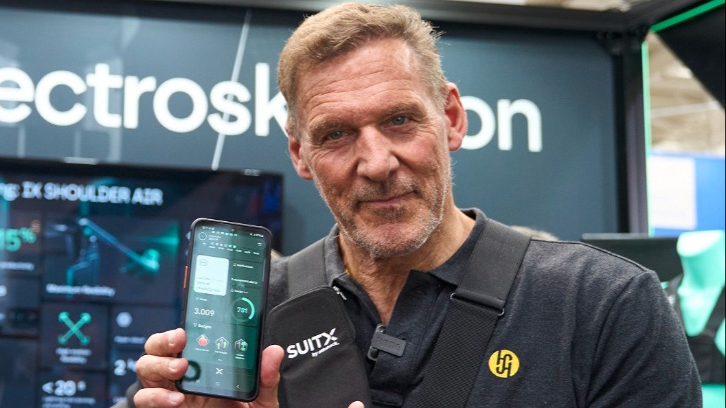Actor Ralf Möller presents a smartphone at the trade show with the AIRGO XP dashboard on its display.