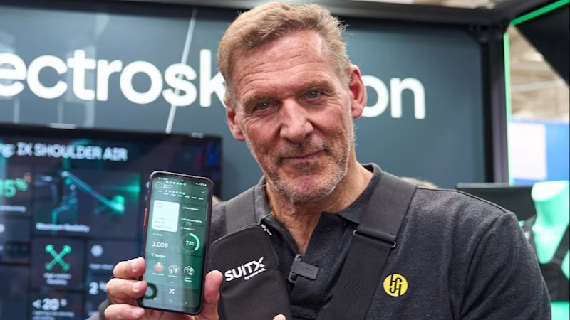 Schauspieler Ralf Möller präsentiert auf der Messe ein Smartphone, auf dessen Display das Dashboard des AIRGO XP zu sehen ist.