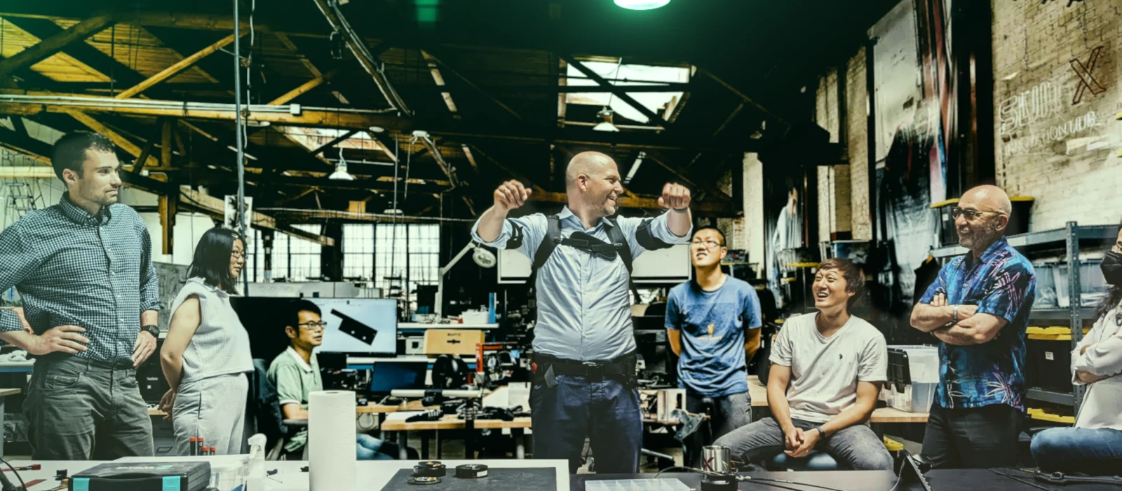 Eine Person in einer Fabrik umgeben von Technikern demonstriert die Funktion eines SUITX Exoskelettes