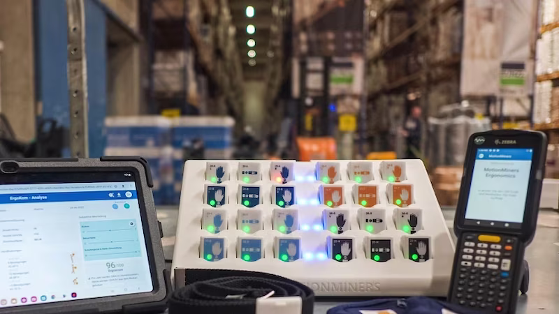 On a table in a warehouse is a tablet with a data dashboard, a pallet with digital stamps and an electronic handheld device.