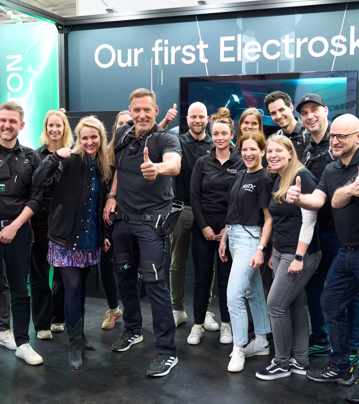 Eine Gruppe Menschen und Ralf Möller präsentieren den Hannover Messe Stand von SUITX by Ottobock.